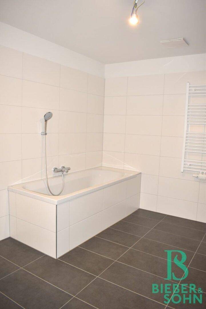 Zeitgemäßes Badezimmer mit Badewanne, Handtuchheizkörper und dunklem Fliesenboden.