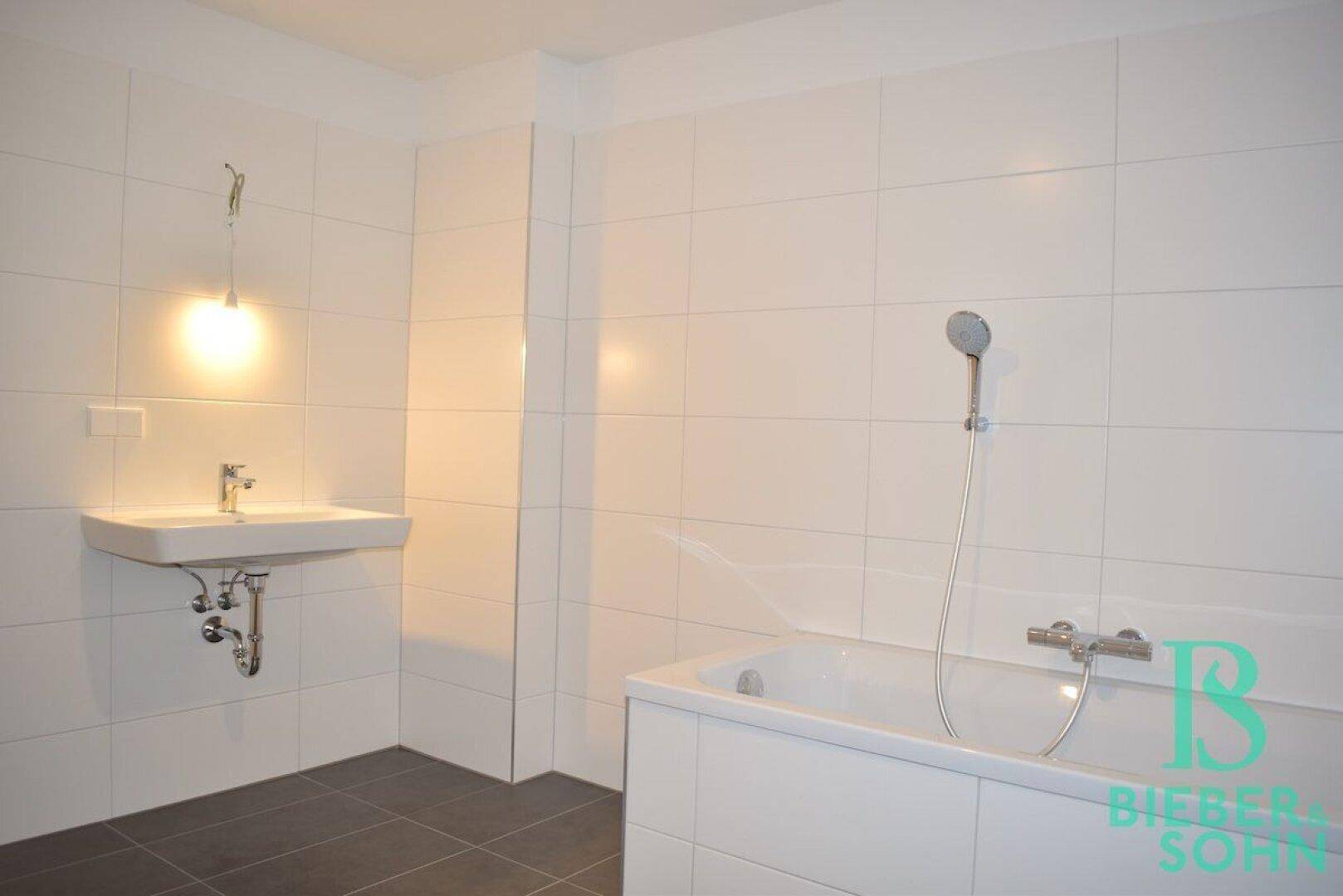 Modern gefliestes Badezimmer mit Badewanne und Waschbecken, in hellen Farbtönen gehalten.