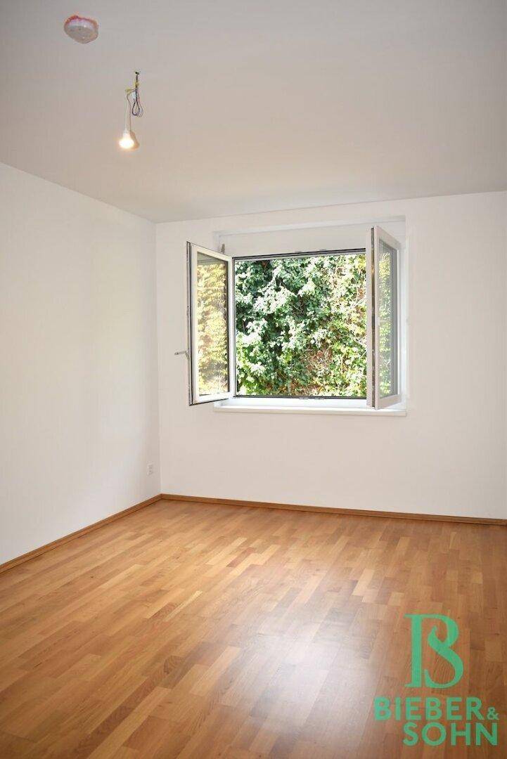Freundliches Zimmer mit Holzboden und geöffnetem Fenster, das viel Tageslicht hereinlässt.
