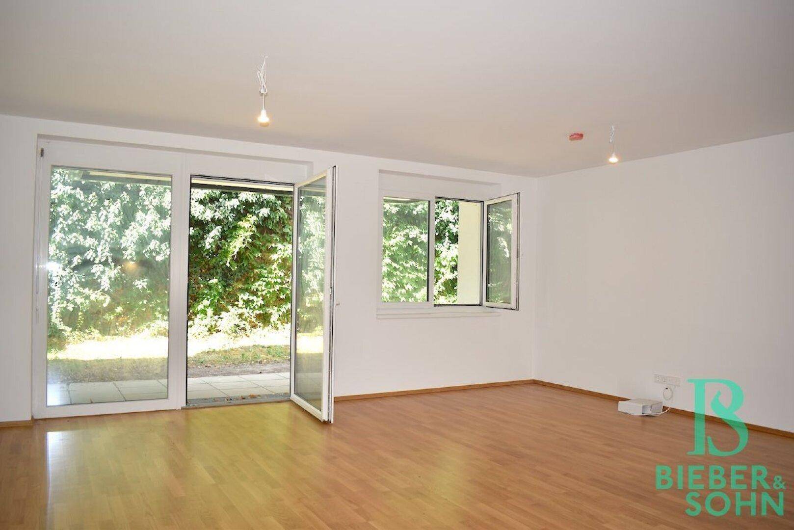 Helles Wohnzimmer mit großen Fenstern, Parkettboden und direktem Zugang zum Garten.
