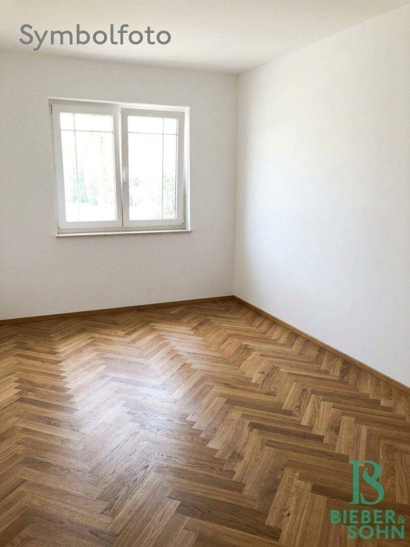 Leeres Zimmer mit Fischgrätparkett und einem Fenster, das viel Tageslicht hereinlässt.