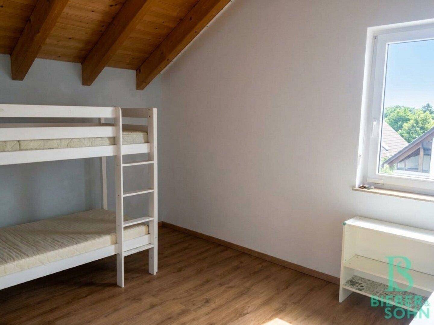 Kinderzimmer im Dachgeschoss mit Etagenbett, Holzboden und einem Fenster mit Ausblick.
