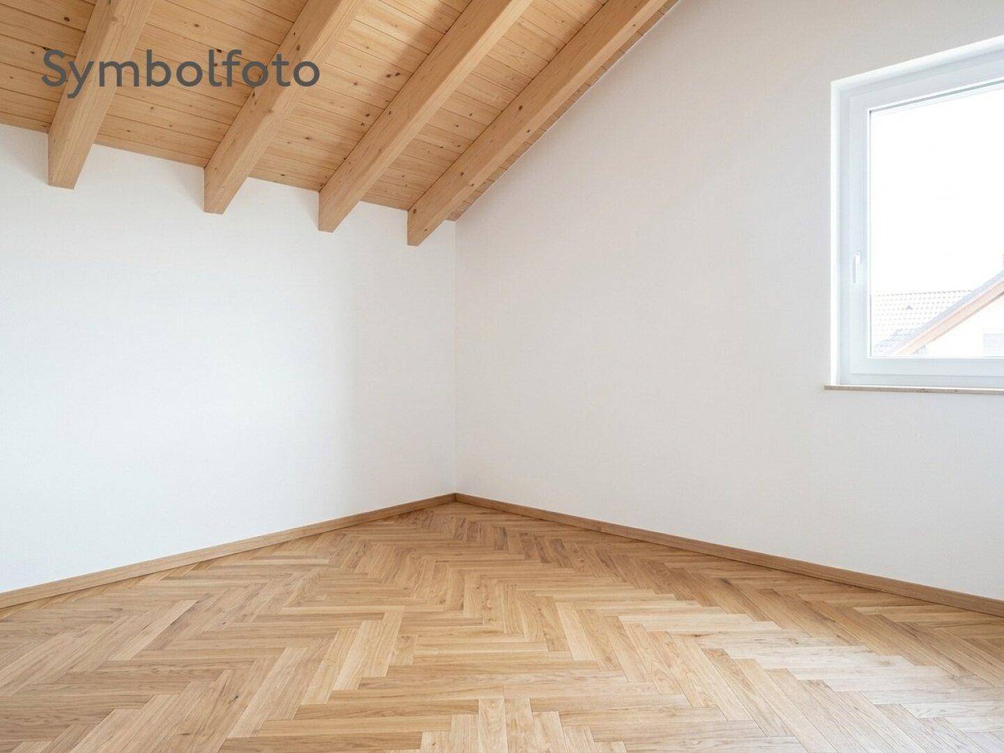 Leeres Schlafzimmer im Dachgeschoss mit Fischgrätparkett und sichtbaren Holzbalken.