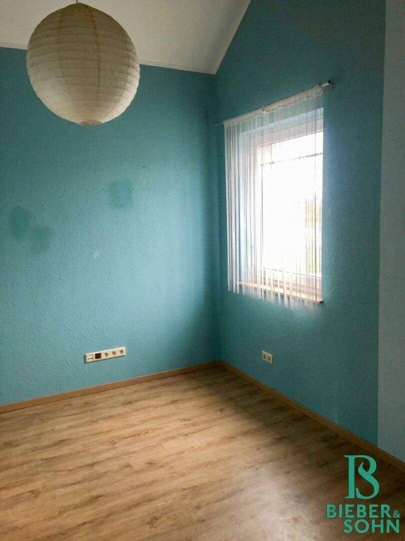 Schlafzimmer mit blaugrünen Wänden, Holzboden und einem Fenster, das viel Licht hereinlässt.