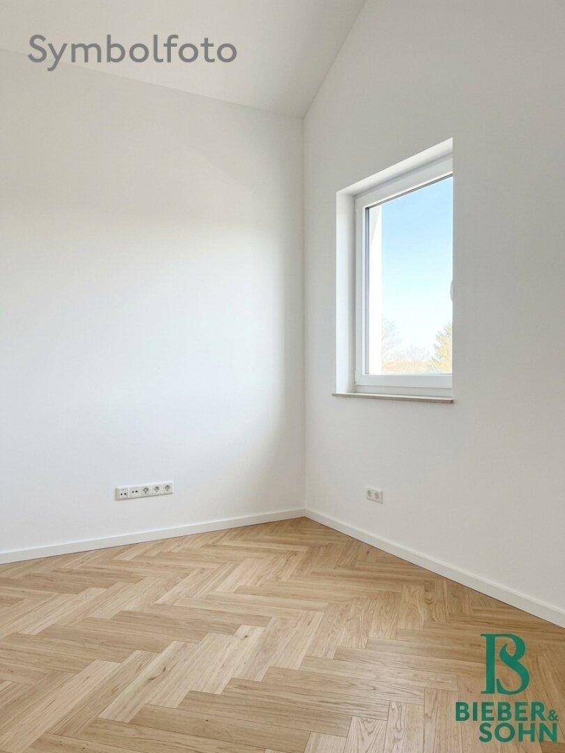 Helles, leeres Zimmer mit Fischgrätparkett und einem Fenster, das den Raum gut belichtet.