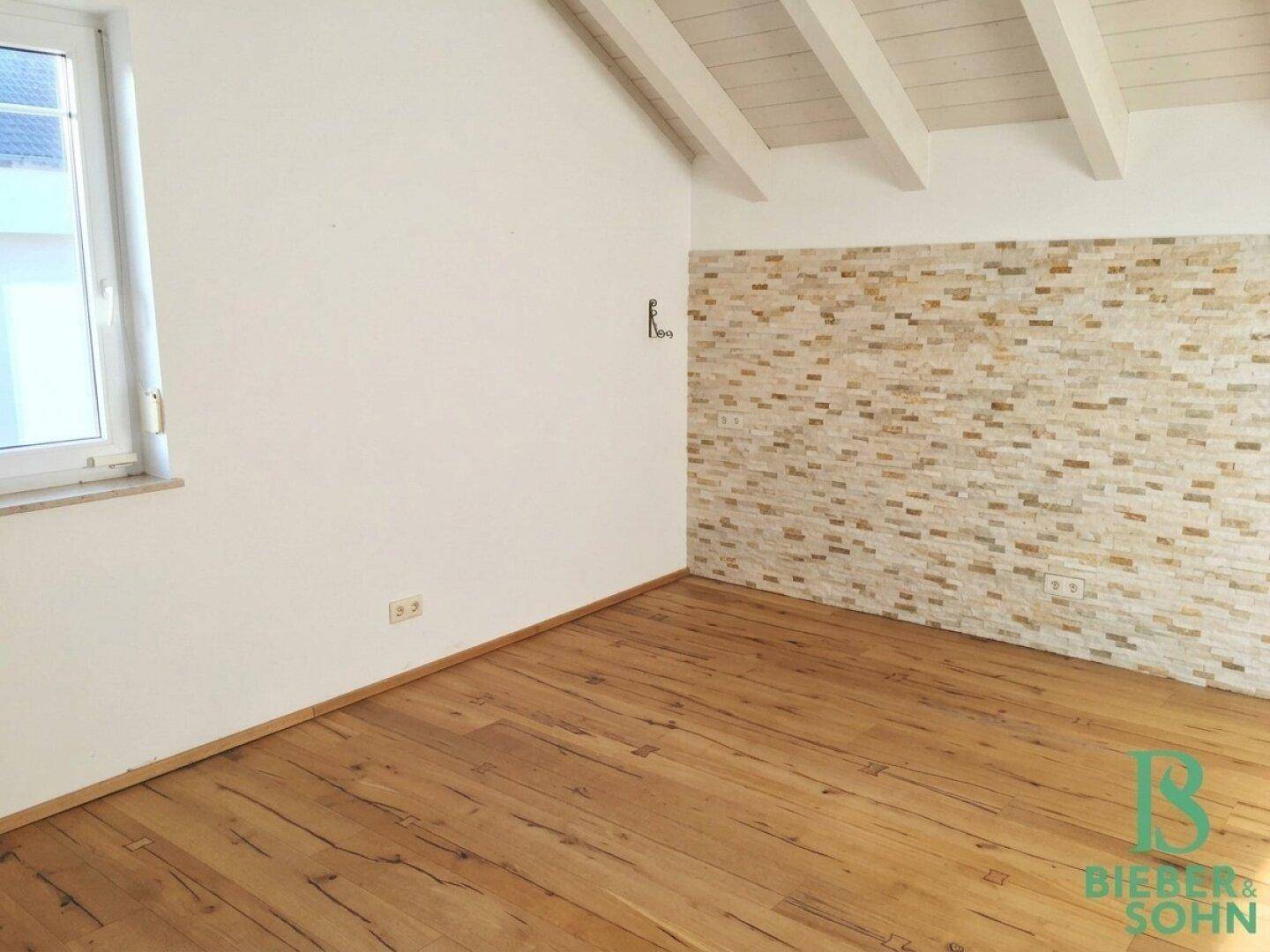 Schlafzimmer im Dachgeschoss mit Holzboden, einer Steinwand und sichtbaren Holzbalken.