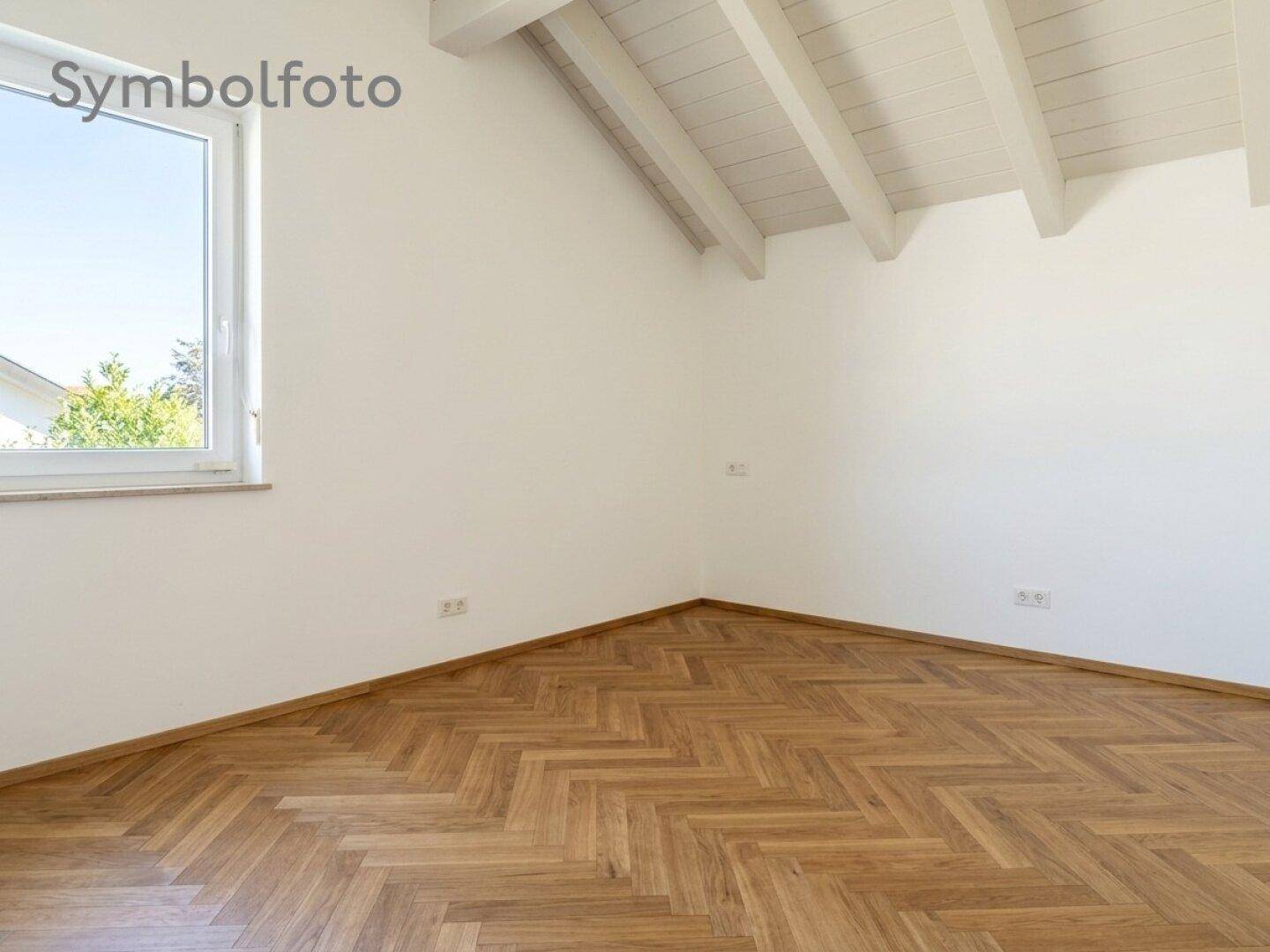 Leeres Schlafzimmer im Dachgeschoss mit Fischgrätparkett und sichtbaren Holzbalken.