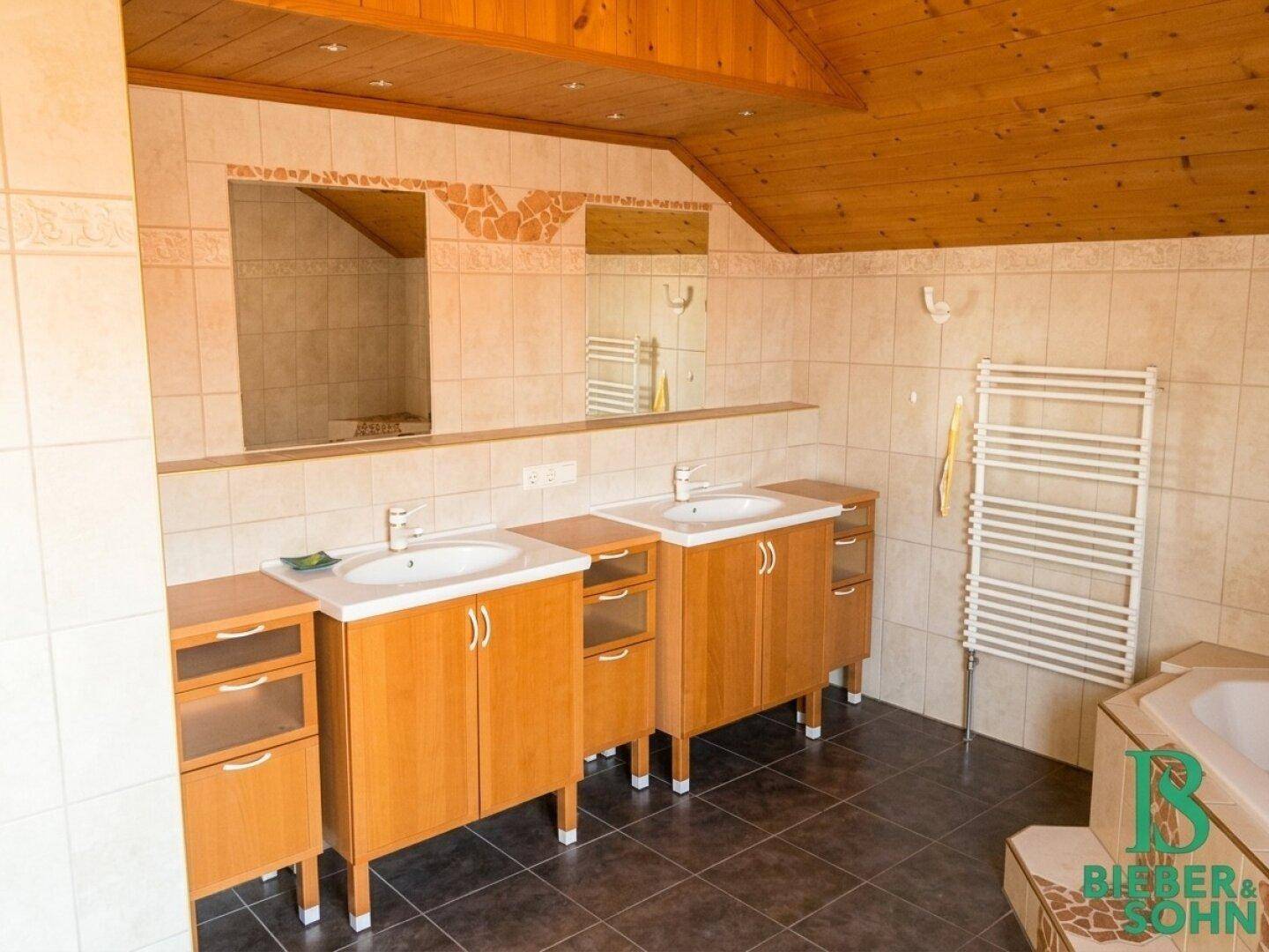 Geräumiges Badezimmer im Dachgeschoss mit zwei Waschbecken, Badewanne und Holzdecke.