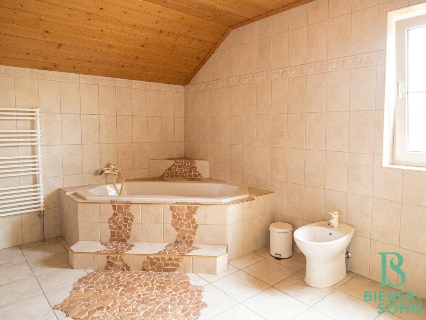 Badezimmer mit Eckbadewanne, Bidet, Fenster und gefliestem Boden im Dachgeschoss.