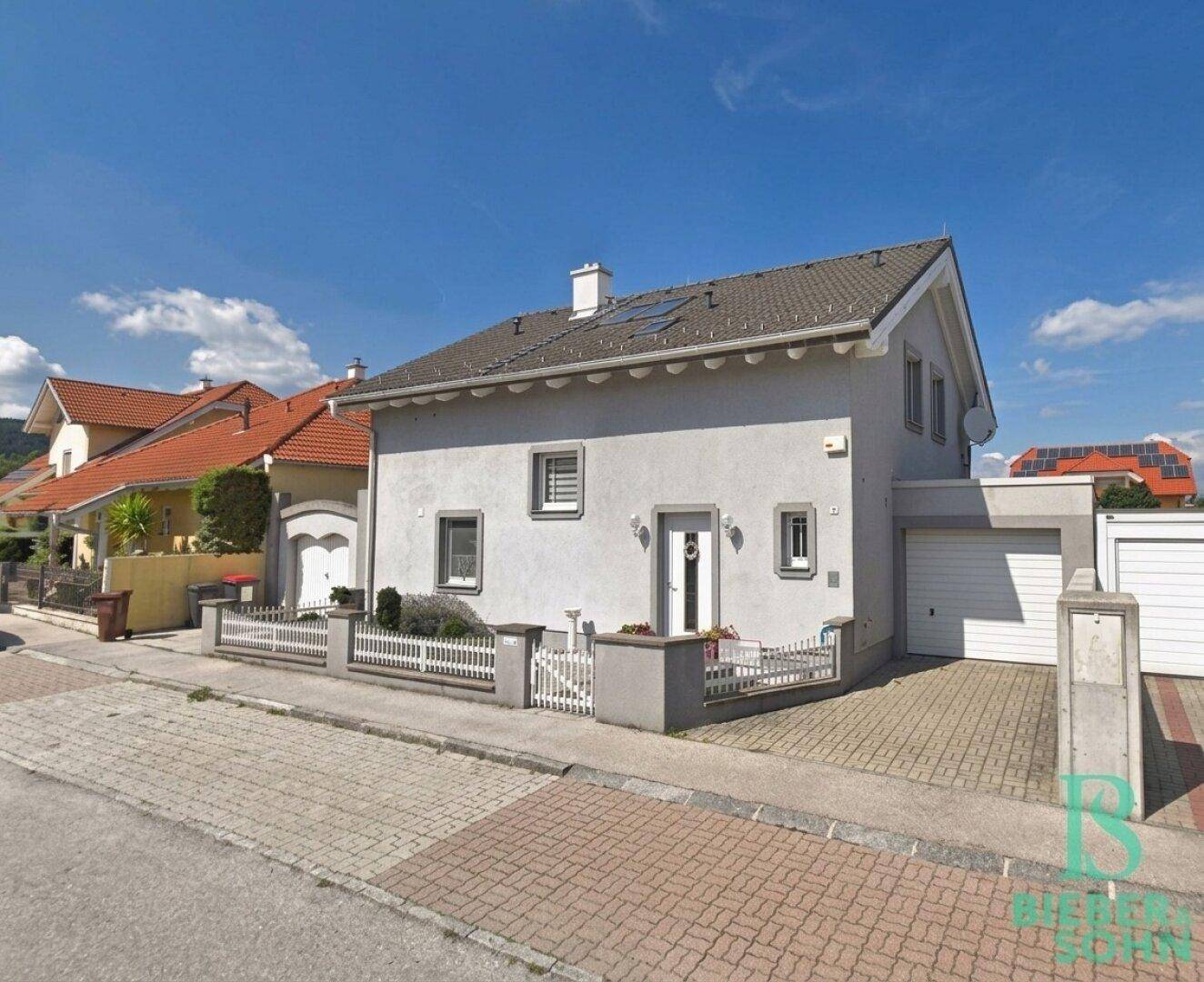 Einfamilienhaus mit grauer Fassade, Vorgarten und Garage an einer Wohnstraße.