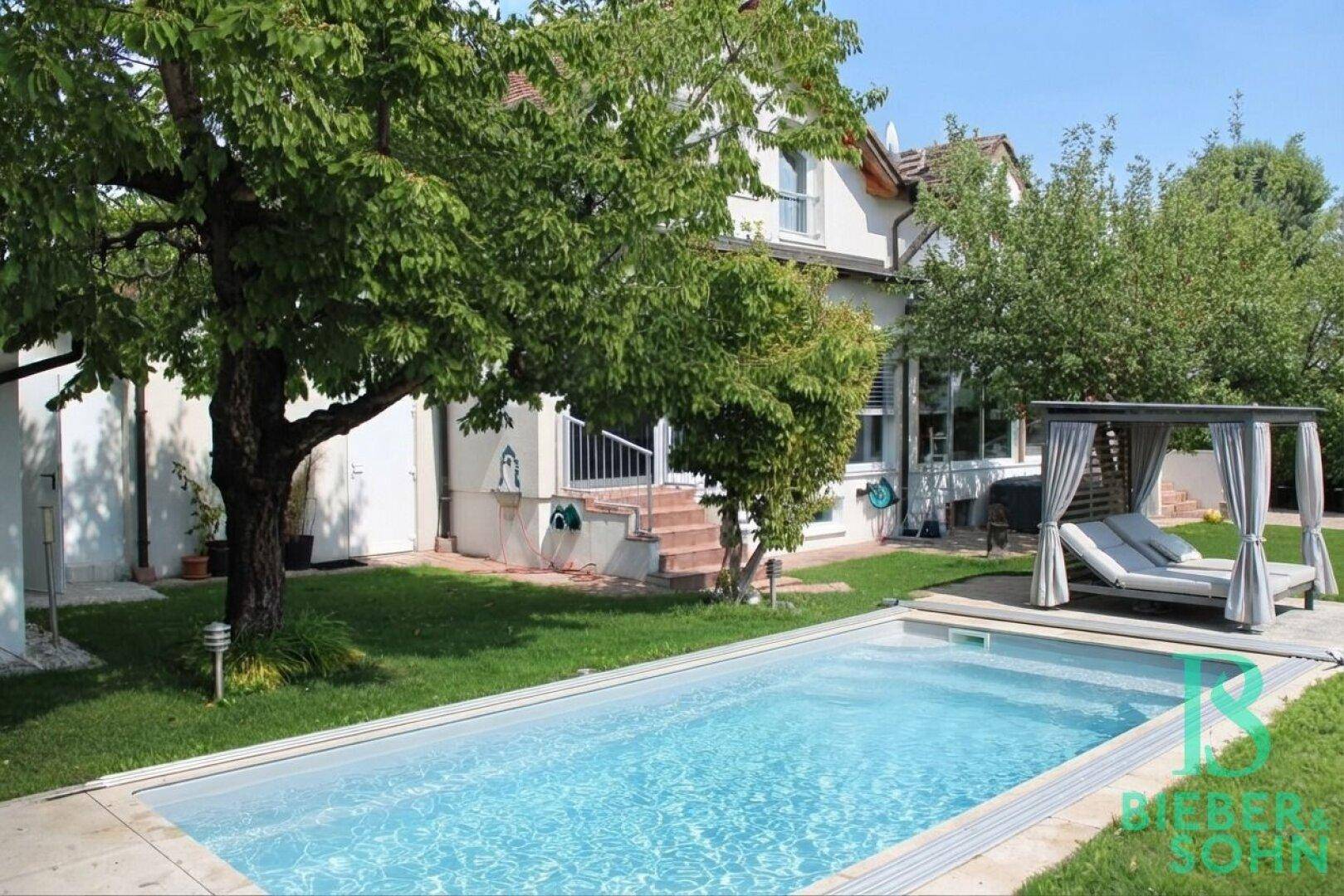 Weitläufiger Garten mit Schwimmbecken, Liegefläche und altem Baumbestand.