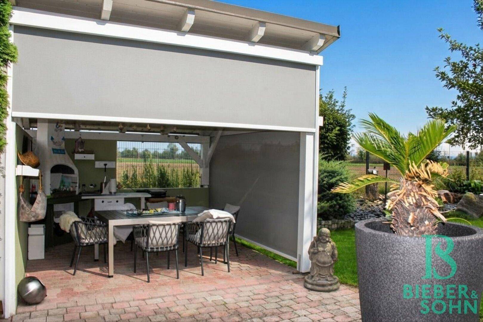 Überdachte Terrasse mit Außenküche, Essbereich und Blick ins Grüne.