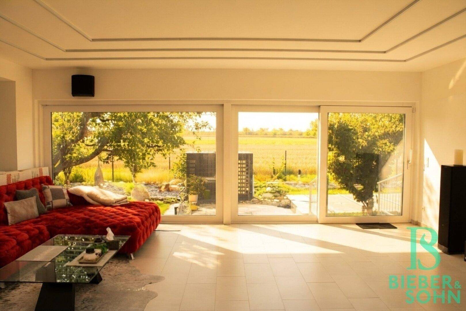 Lichtdurchflutetes Wohnzimmer mit rotem Sofa und weitem Blick ins Grüne.