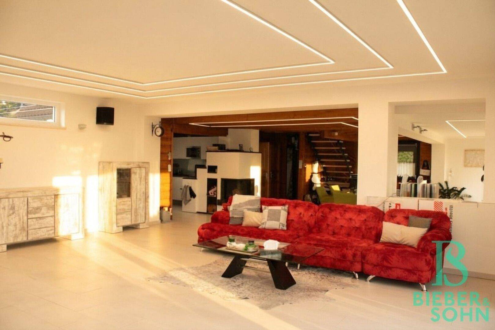 Offener Wohnbereich mit rotem Sofa, Kamin und Zugang zum Essbereich.