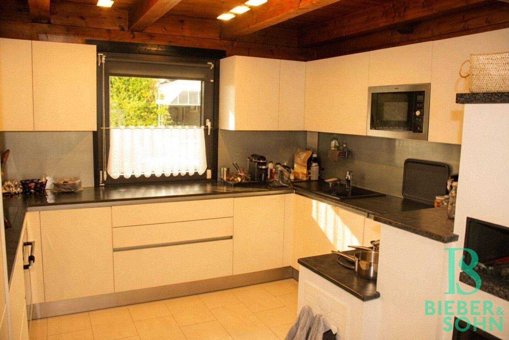 Helle Küche mit weißen Schränken, dunkler Arbeitsplatte und Fensterblick.