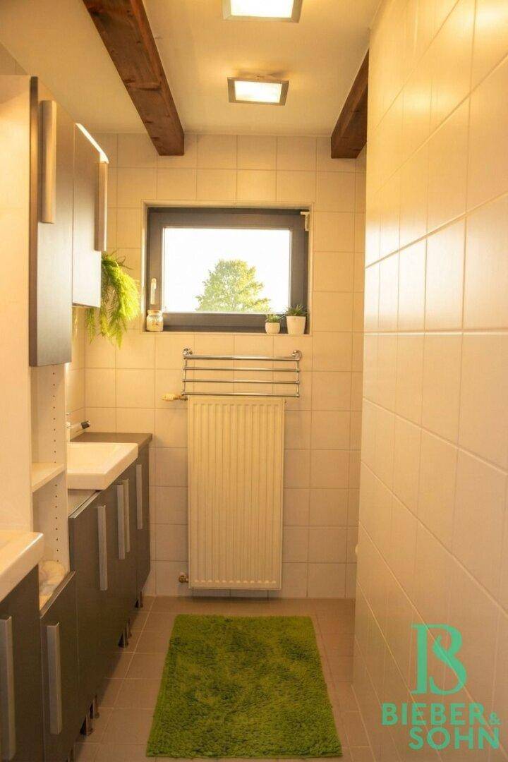 Helles Badezimmer mit Fenster, Waschbecken und Handtuchheizkörper.