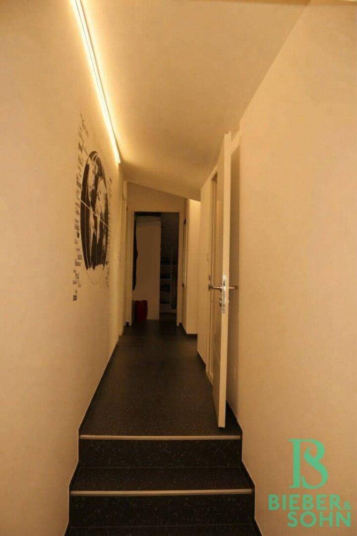 Langer Flur mit dunklem Boden und Treppe zu weiteren Räumen.
