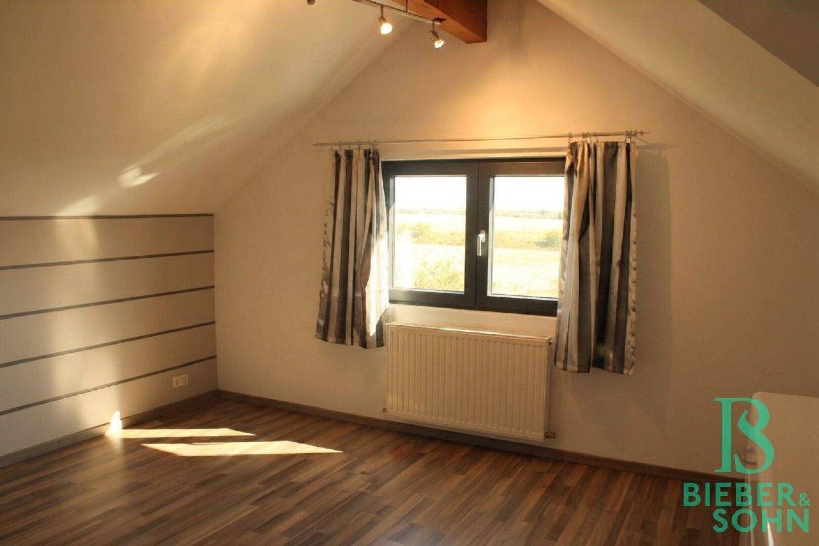 Helles Schlafzimmer im Dachgeschoss mit Holzboden und Blick ins Grüne.
