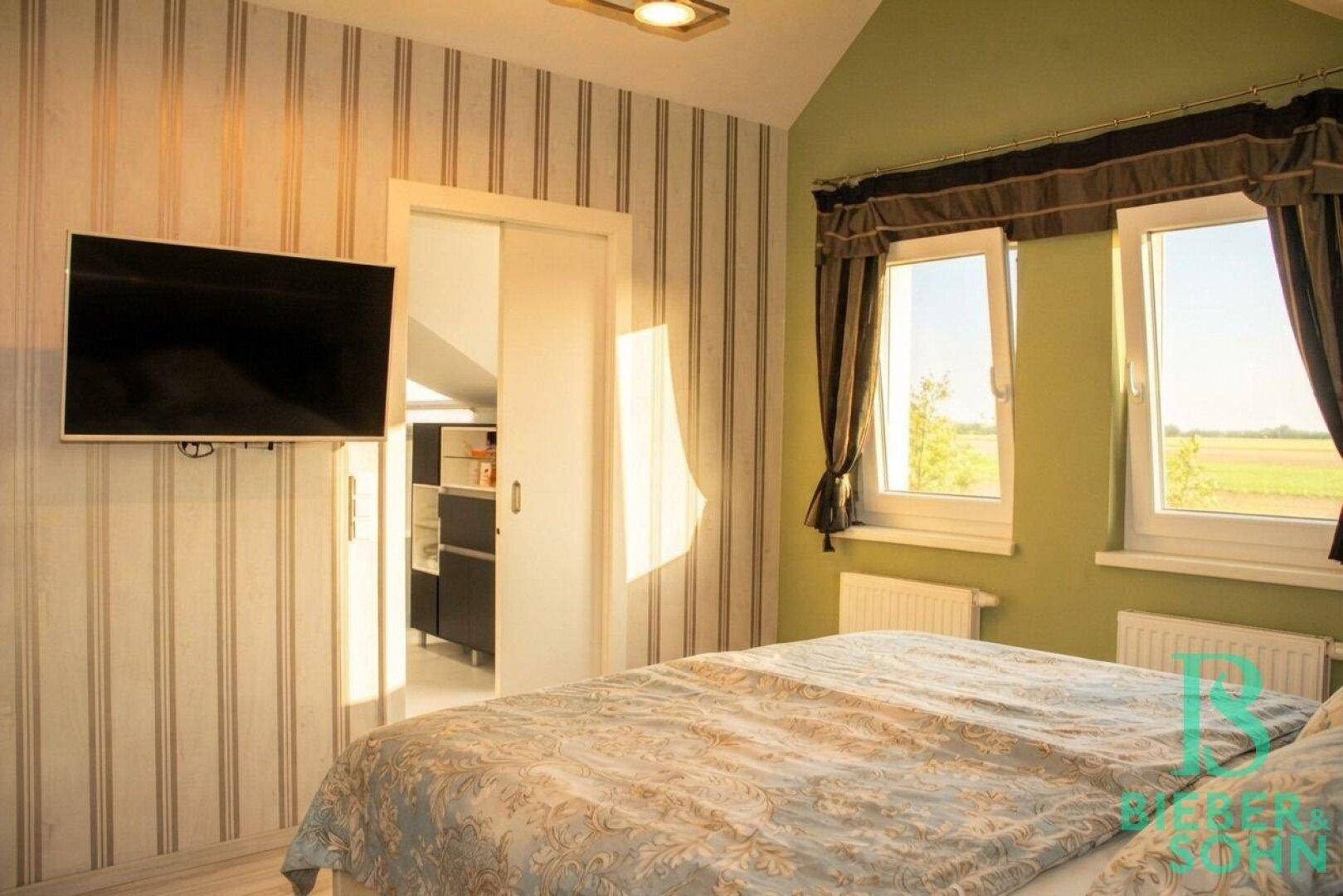 Gemütliches Schlafzimmer mit gestreifter Tapete, Fernseher und Zugang zu einem Ankleidezimmer.