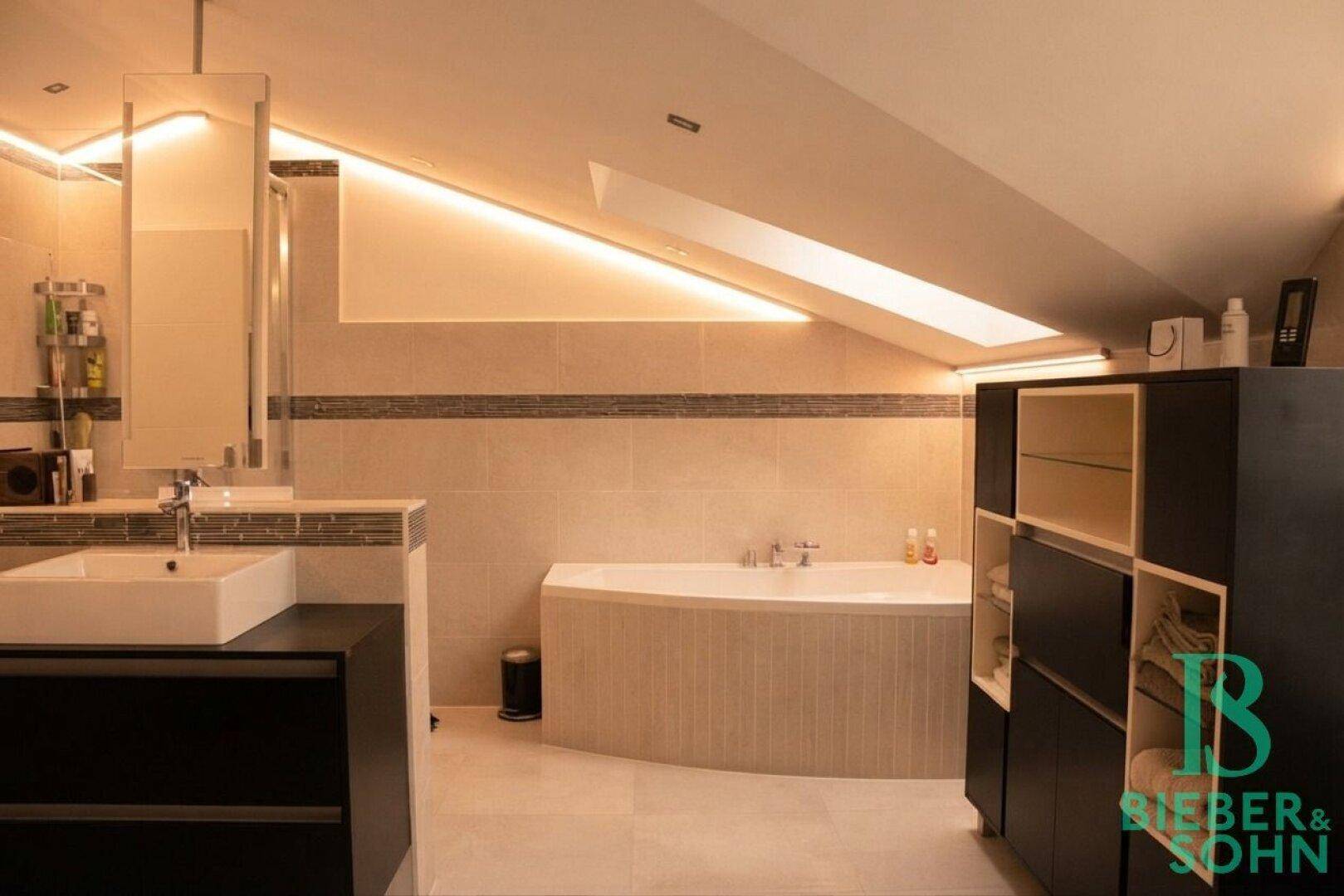 Modernes Badezimmer mit Badewanne, Doppelwaschbecken und indirekter Beleuchtung unter der Dachschräge.