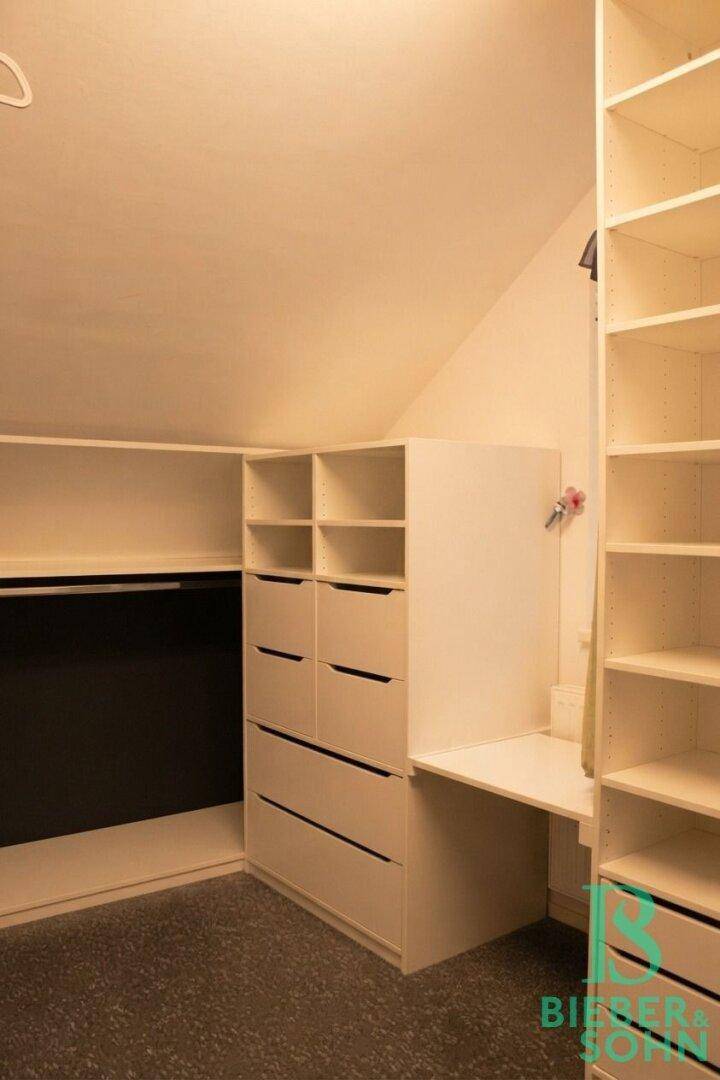 Praktisches Ankleidezimmer mit maßgefertigten Regalen und Schubladen unter der Dachschräge.