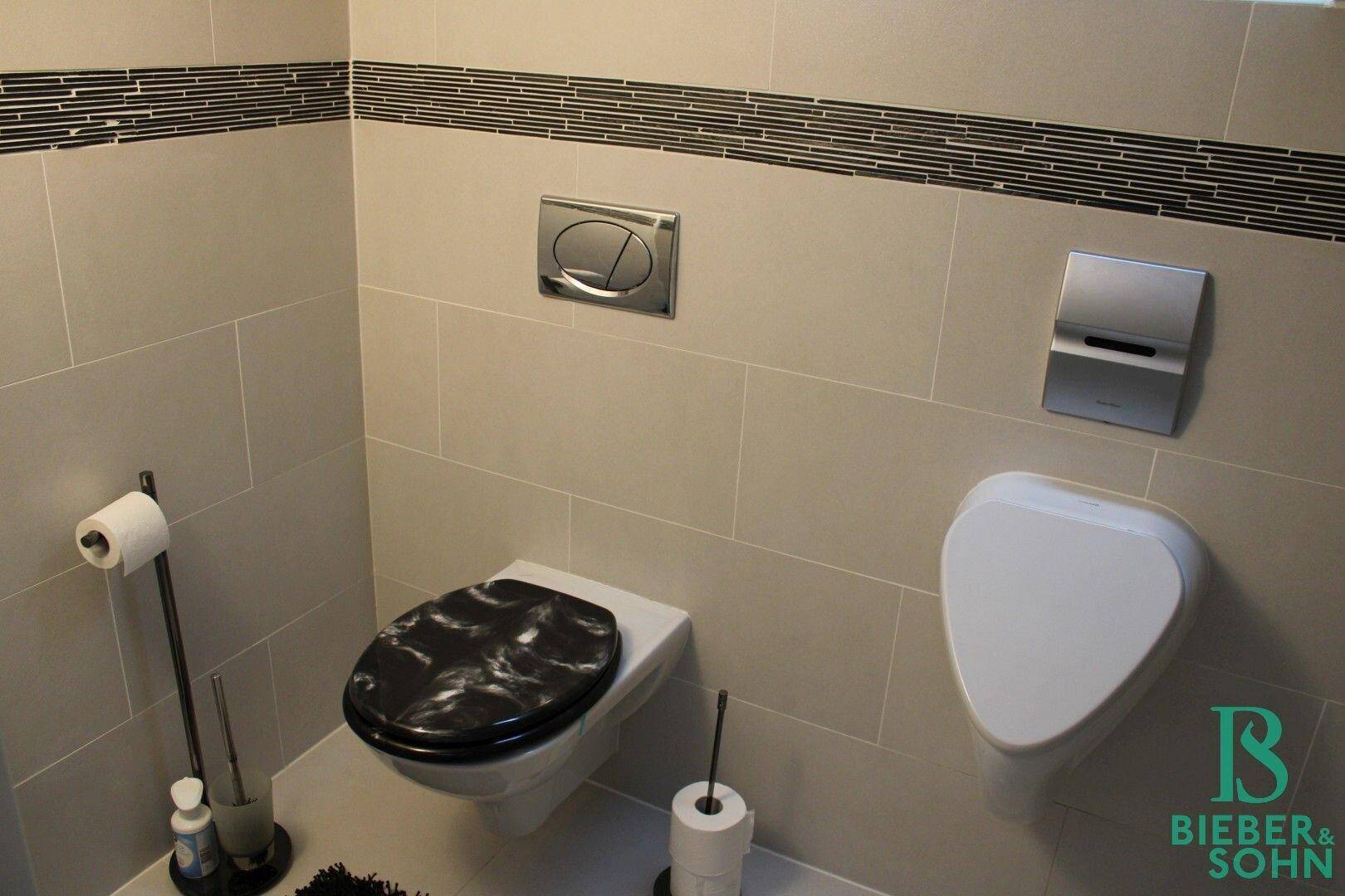 Modernes Gäste-WC mit wandhängender Toilette, Urinal und stilvollen Fliesen.