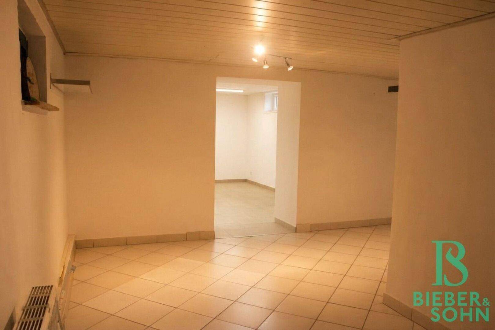 Geräumiger Kellerflur mit Fliesenboden und sichtbaren Holzbalken an der Decke.