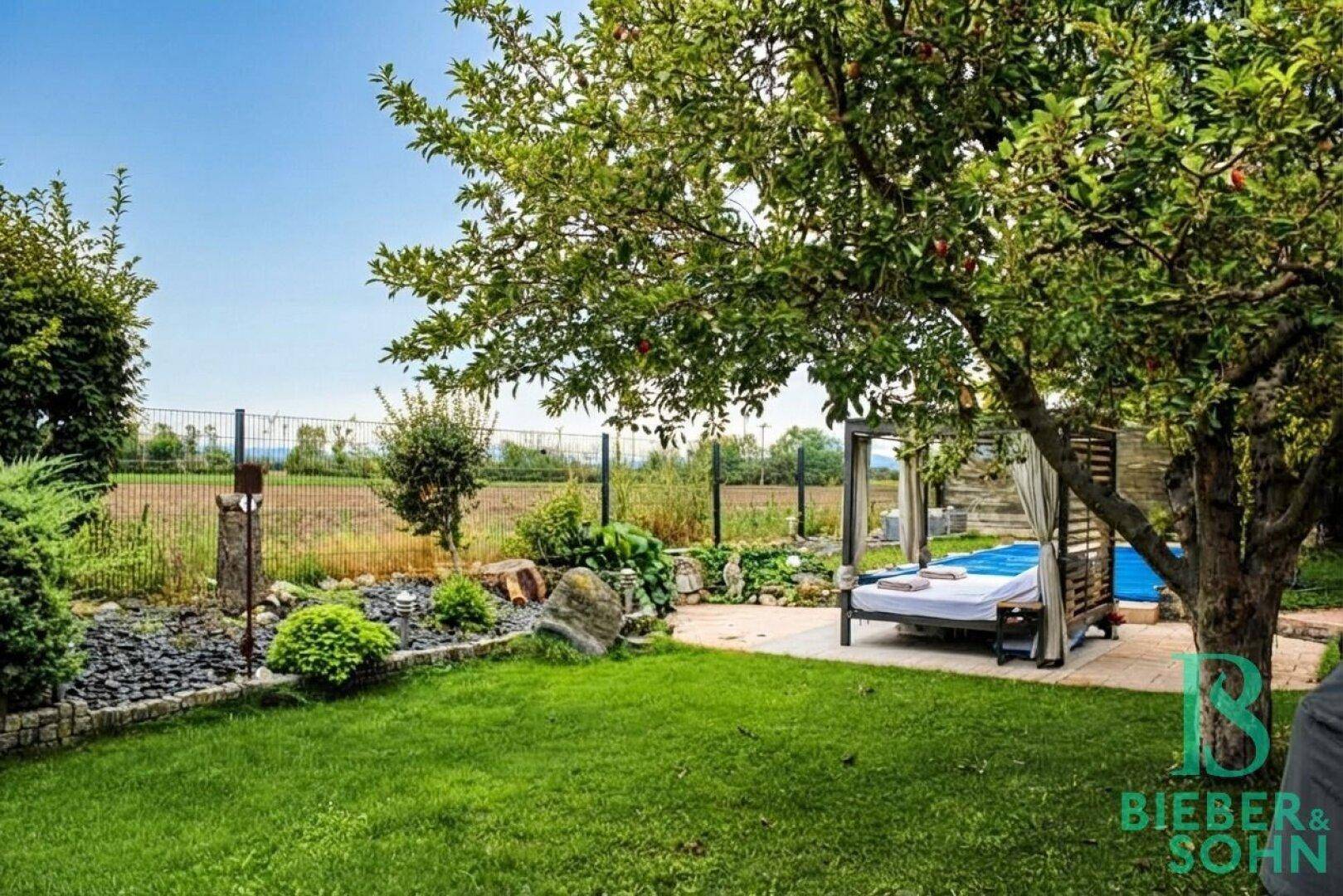 Gepflegter Garten mit Rasenfläche, Obstbäumen, Liegebereich und weitem Blick ins Grüne.