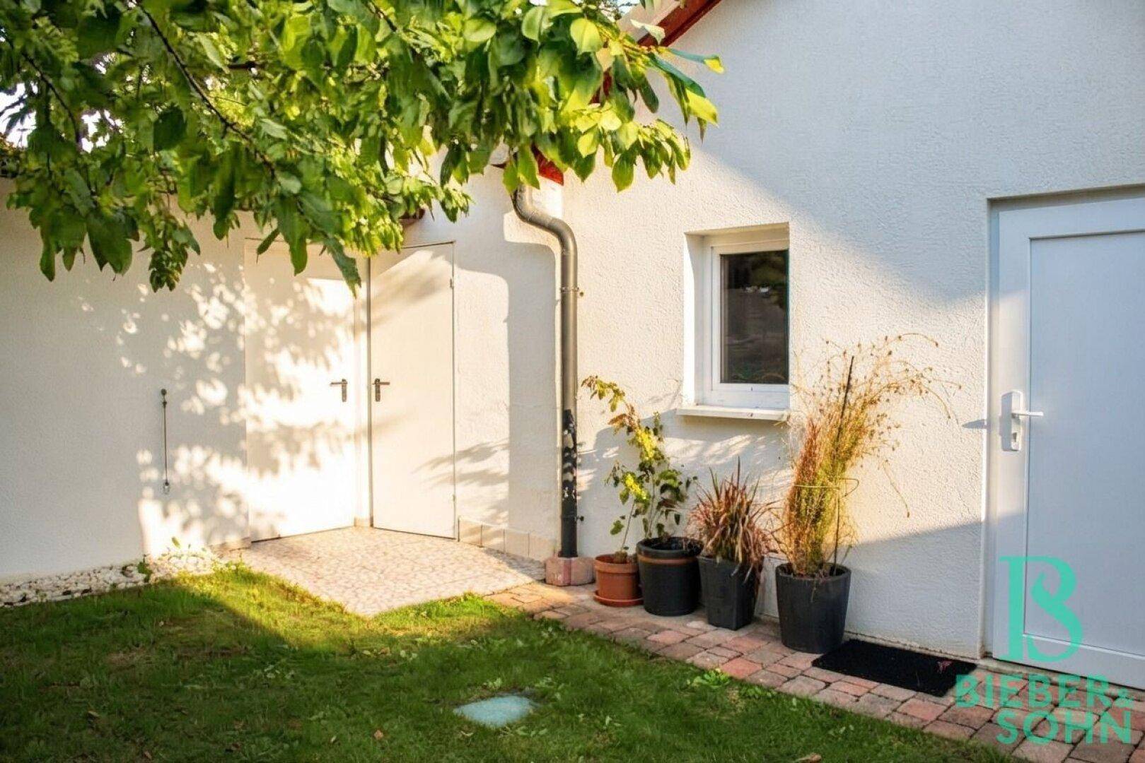 Hausfassade mit zwei Türen, einem Fenster und dekorativen Topfpflanzen im Außenbereich.