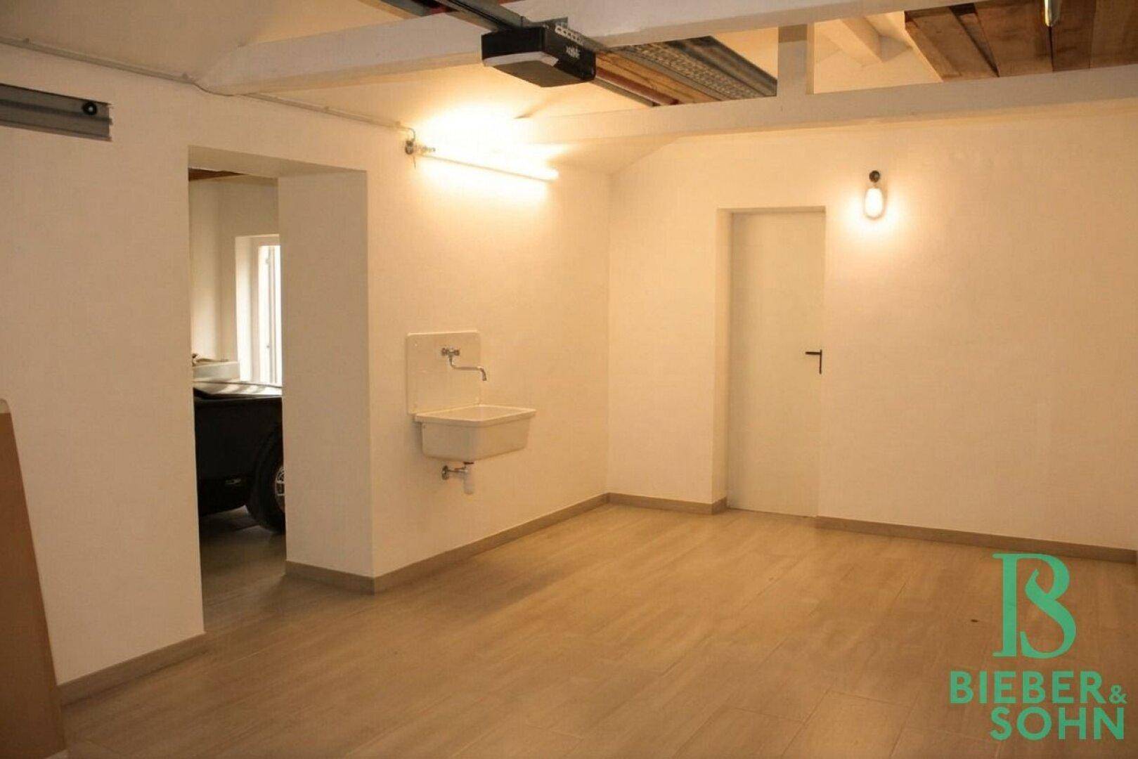 Heller Mehrzweckraum mit Waschbecken, Holzboden und sichtbaren Deckenbalken.