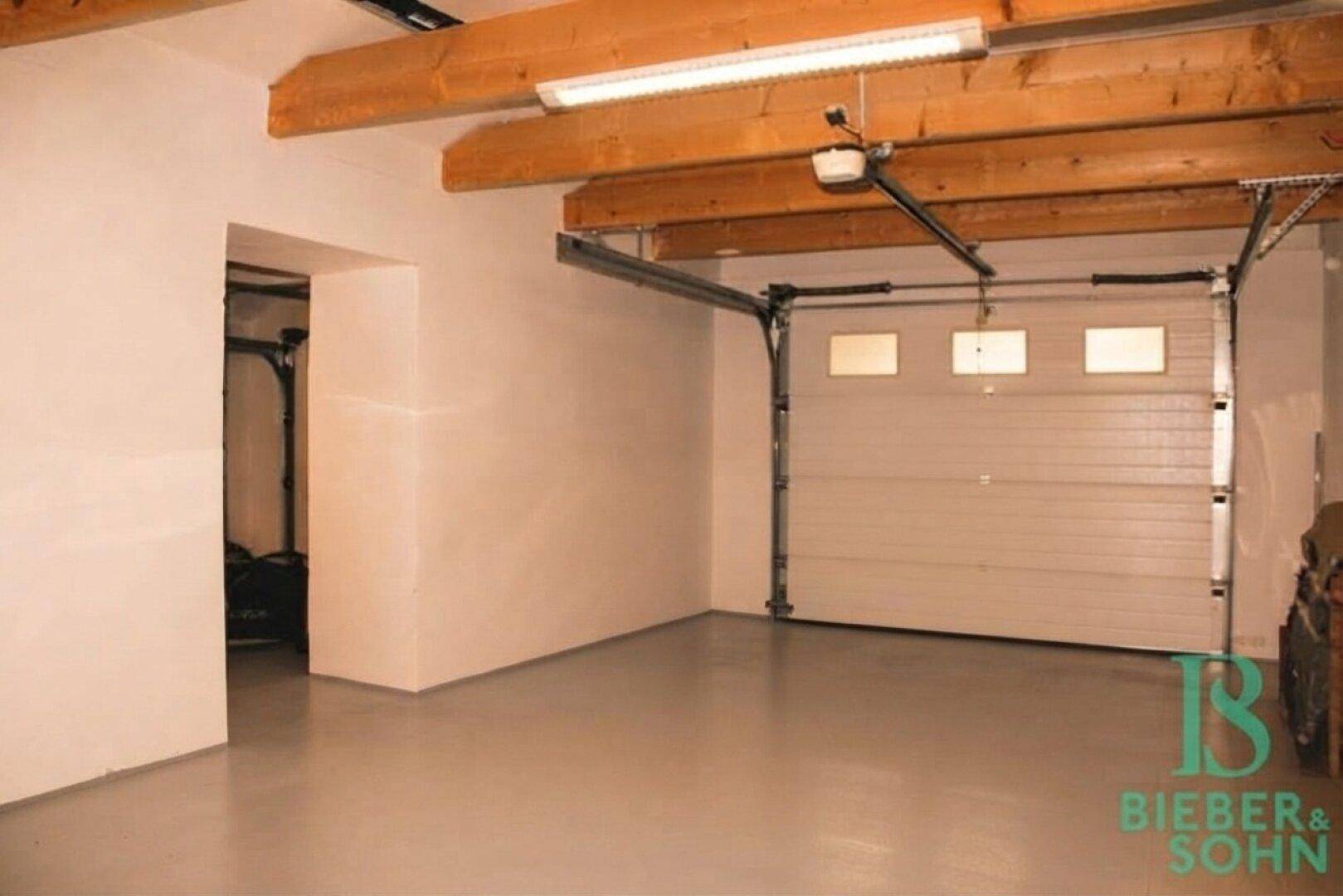 Geräumige Garage mit offenem Garagentor, Betonboden und sichtbaren Holzbalken.