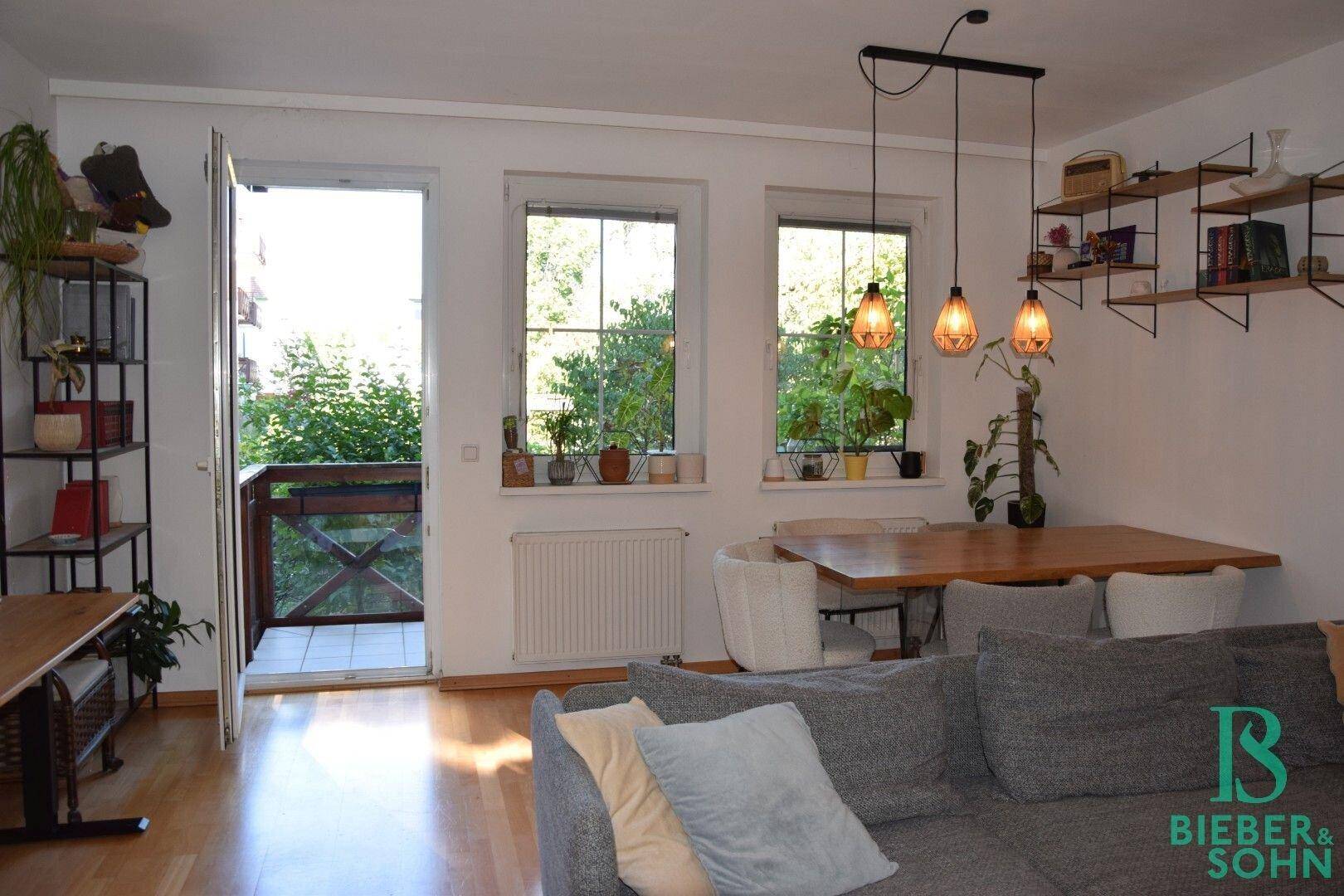 Heller Wohn- und Essbereich mit Holzboden, modernem Sofa und direktem Zugang zum Balkon.