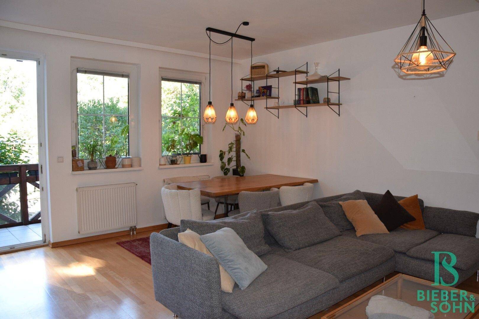Geräumiger Wohn-Essbereich mit hellem Holzboden, gemütlichem Sofa und Blick ins Grüne.
