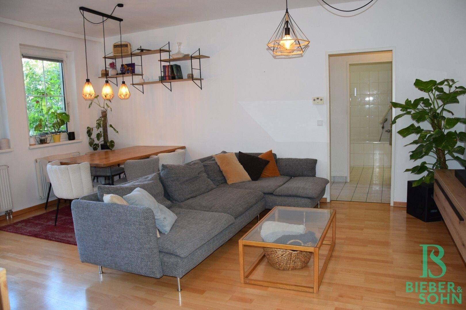 Gemütliches Wohnzimmer mit großem Ecksofa, Holzboden und Zugang zu weiteren Räumen.