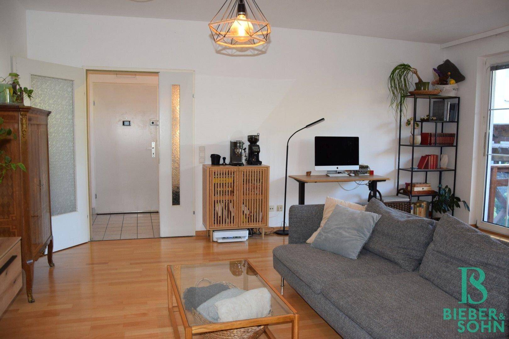 Wohnzimmer mit Arbeitsbereich, Holzboden und Zugang zum Eingangsbereich der Wohnung.