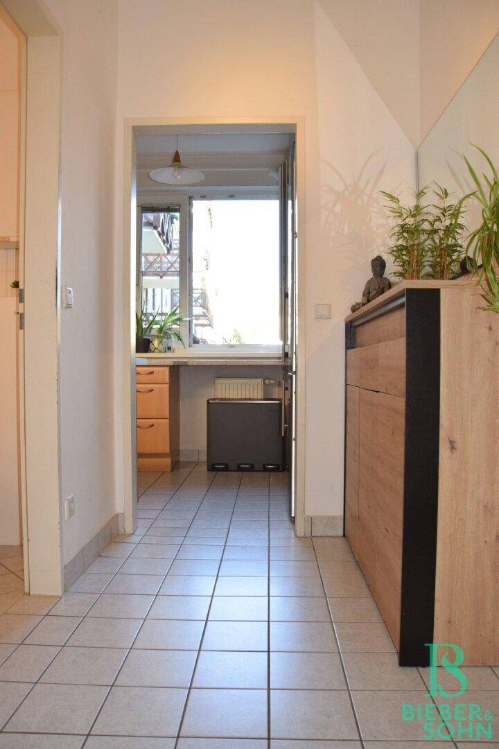 Heller Flur mit Fliesenboden und modernem Holzschrank, der zu weiteren Räumen führt.