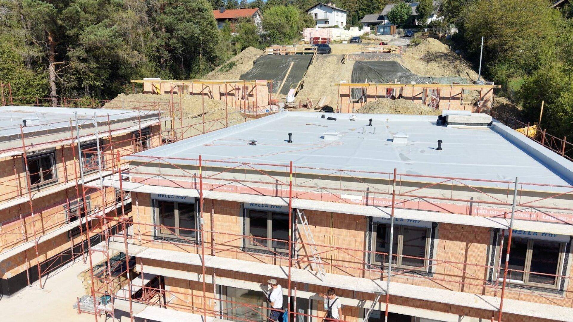 Luftaufnahme einer Baustelle mit mehreren im Bau befindlichen Gebäuden und flachen Dächern.
