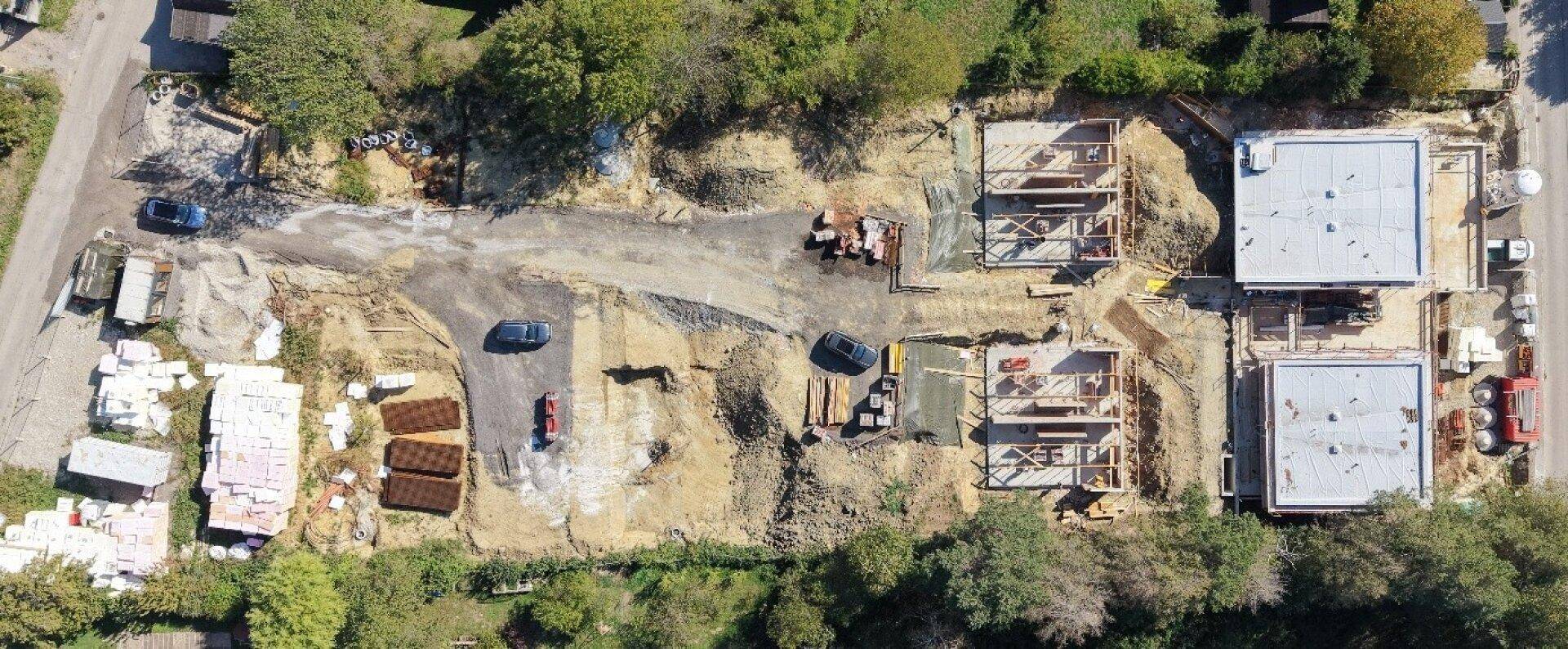 Weitläufige Baustelle aus der Vogelperspektive mit mehreren Gebäudestrukturen und Erdbewegungen.