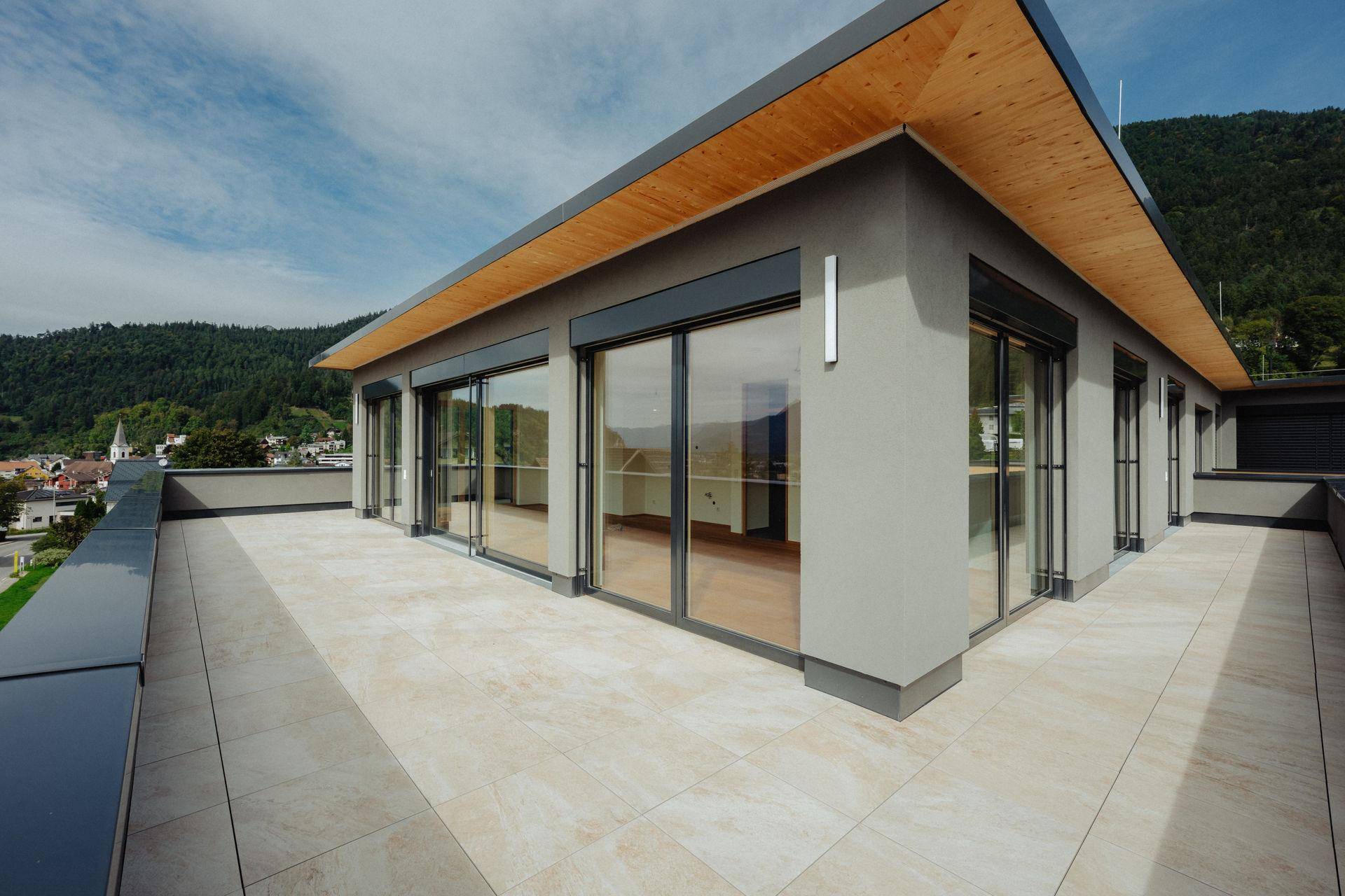 Großzügige Dachterrasse mit Fliesenboden, modernen Fenstern und weitem Ausblick.