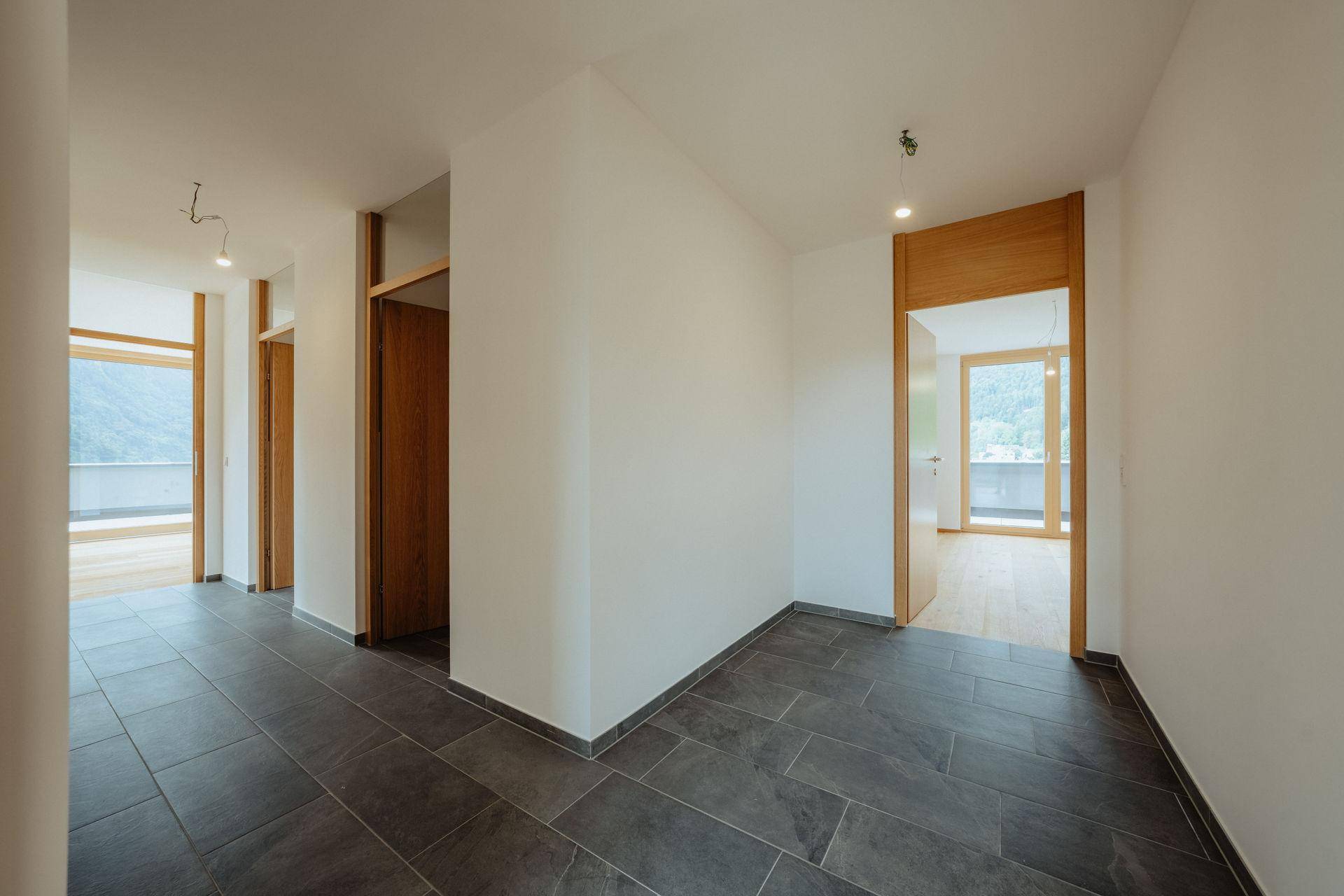 Moderner Flur mit dunklen Fliesen und Holztüren, der zu weiteren Räumen führt.