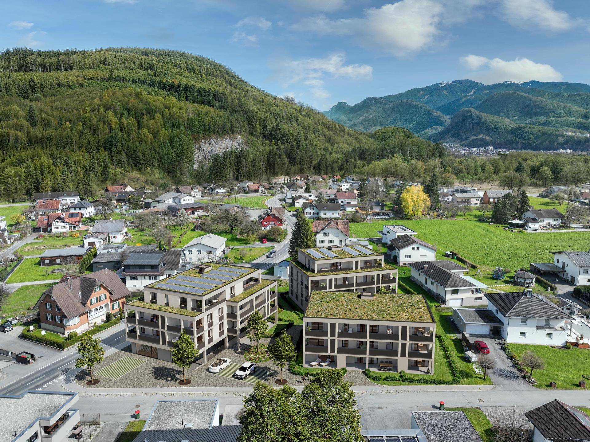 Luftaufnahme einer modernen Wohnanlage in ländlicher Umgebung mit Bergblick und viel Grün.