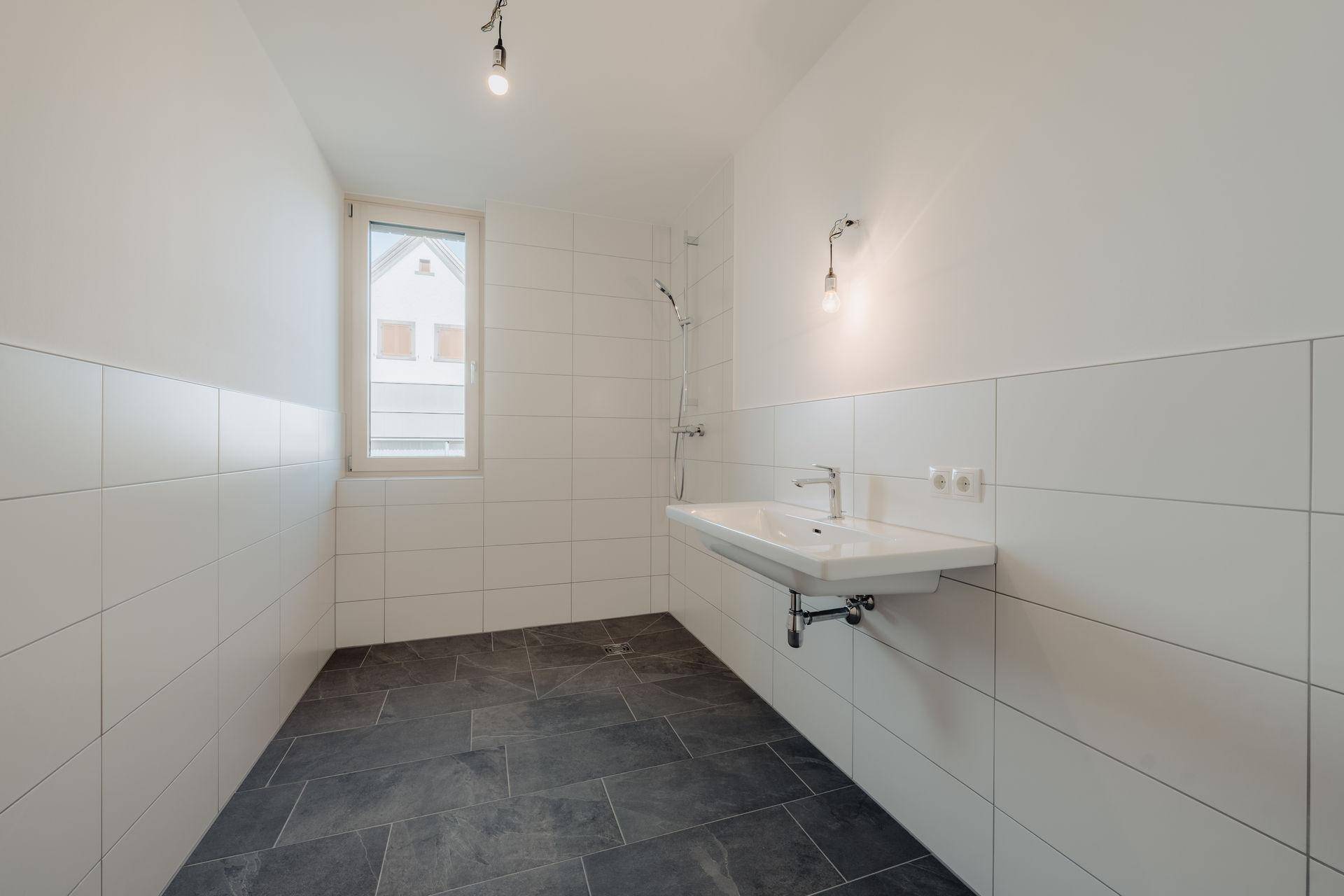 Helles Badezimmer mit weißen Fliesen, dunklem Fliesenboden und einer modernen Dusche.
