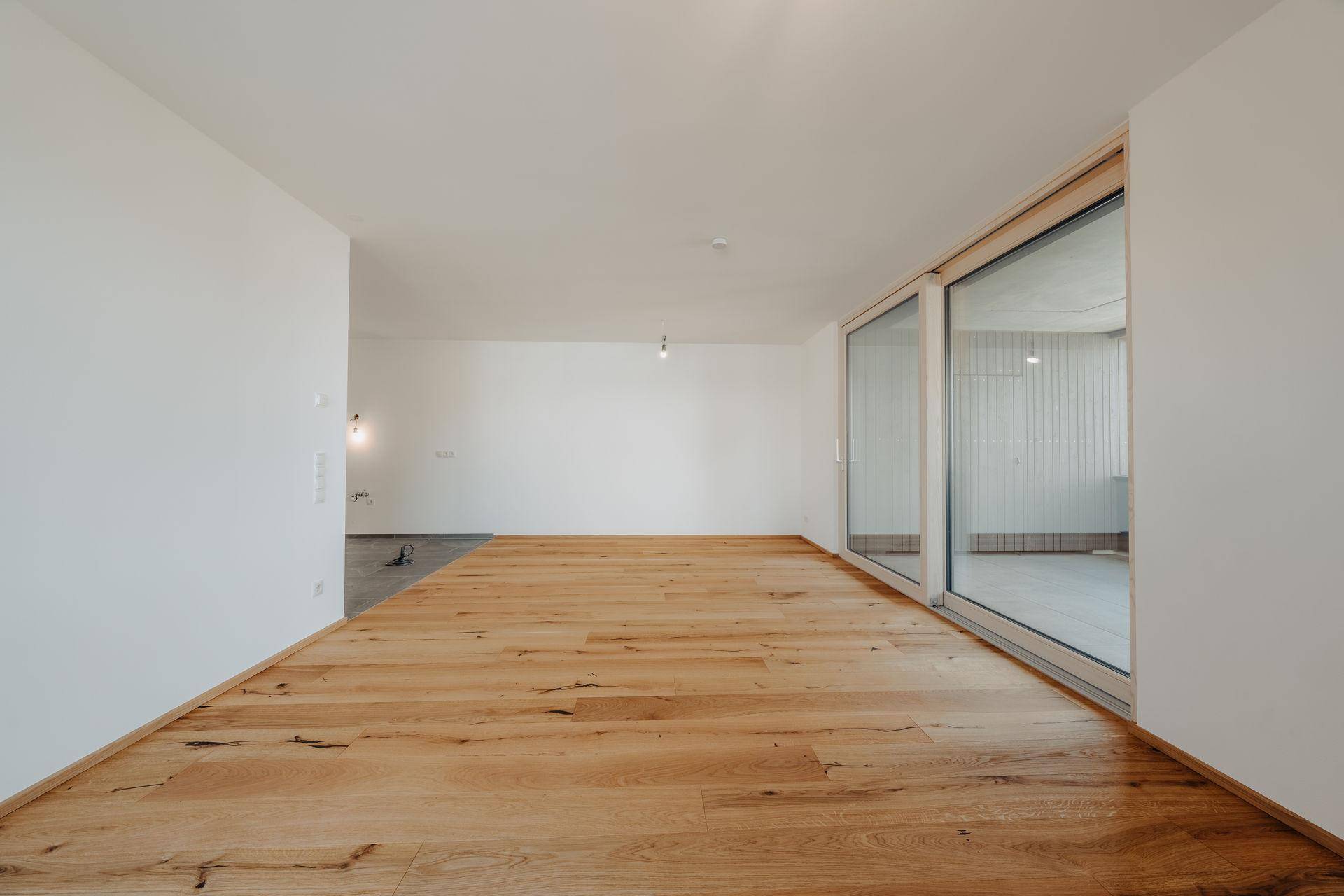 Geräumiger, heller Wohnbereich mit Echtholzparkett und großen Schiebetüren zu einem Balkon.