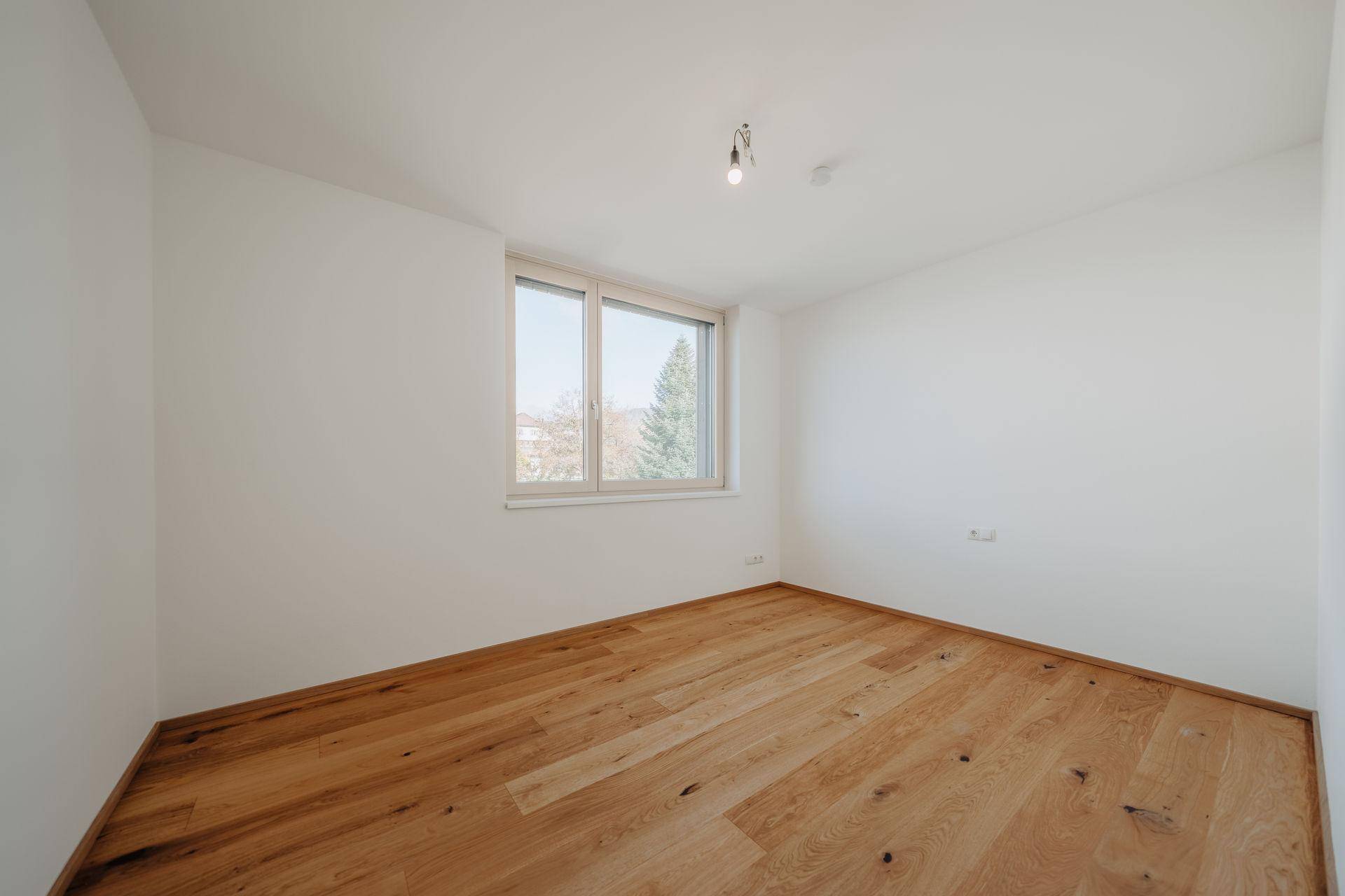Helles Schlafzimmer mit Holzboden und einem großen Fenster, das viel Tageslicht hereinlässt.