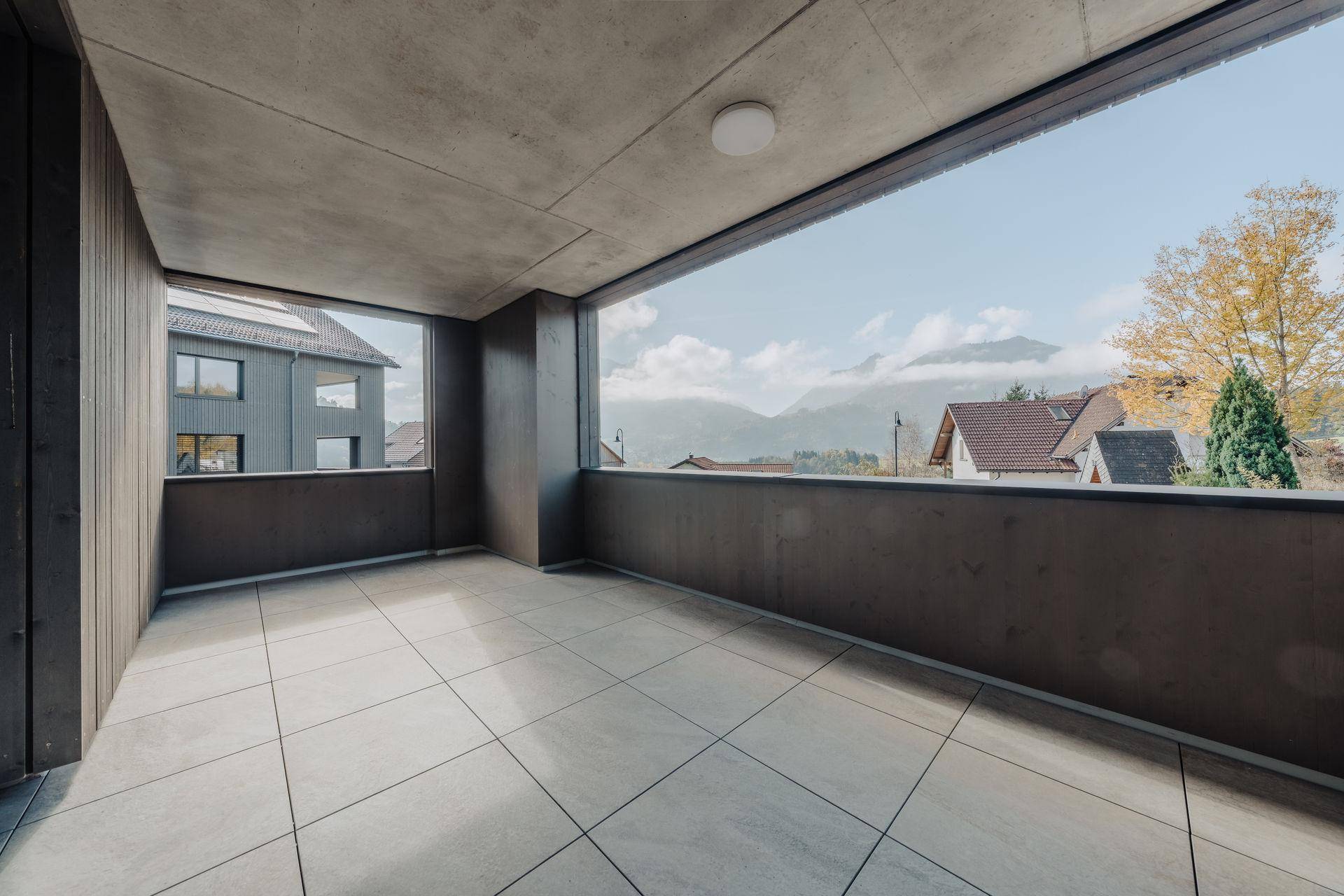 Überdachter Balkon mit Fliesenboden und weitem Blick auf die umliegende Landschaft und Berge.