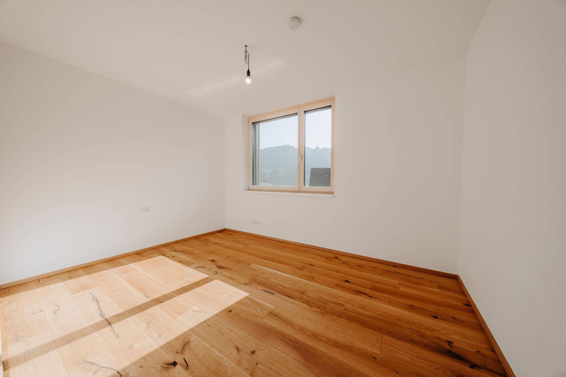 Helles Schlafzimmer mit breiten Holzplankenböden und einem Fenster, das viel Tageslicht hereinlässt.