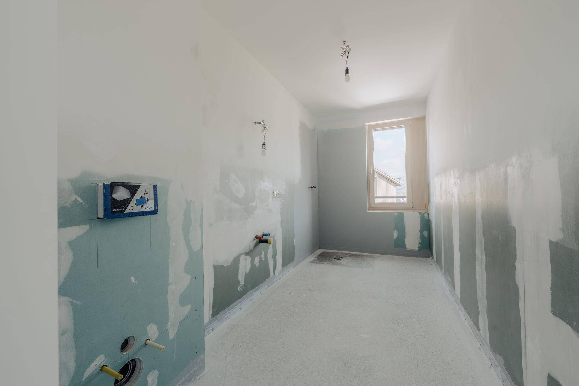 Unfertiges Badezimmer mit Fenster und sichtbaren Installationen, bereit für den Ausbau.