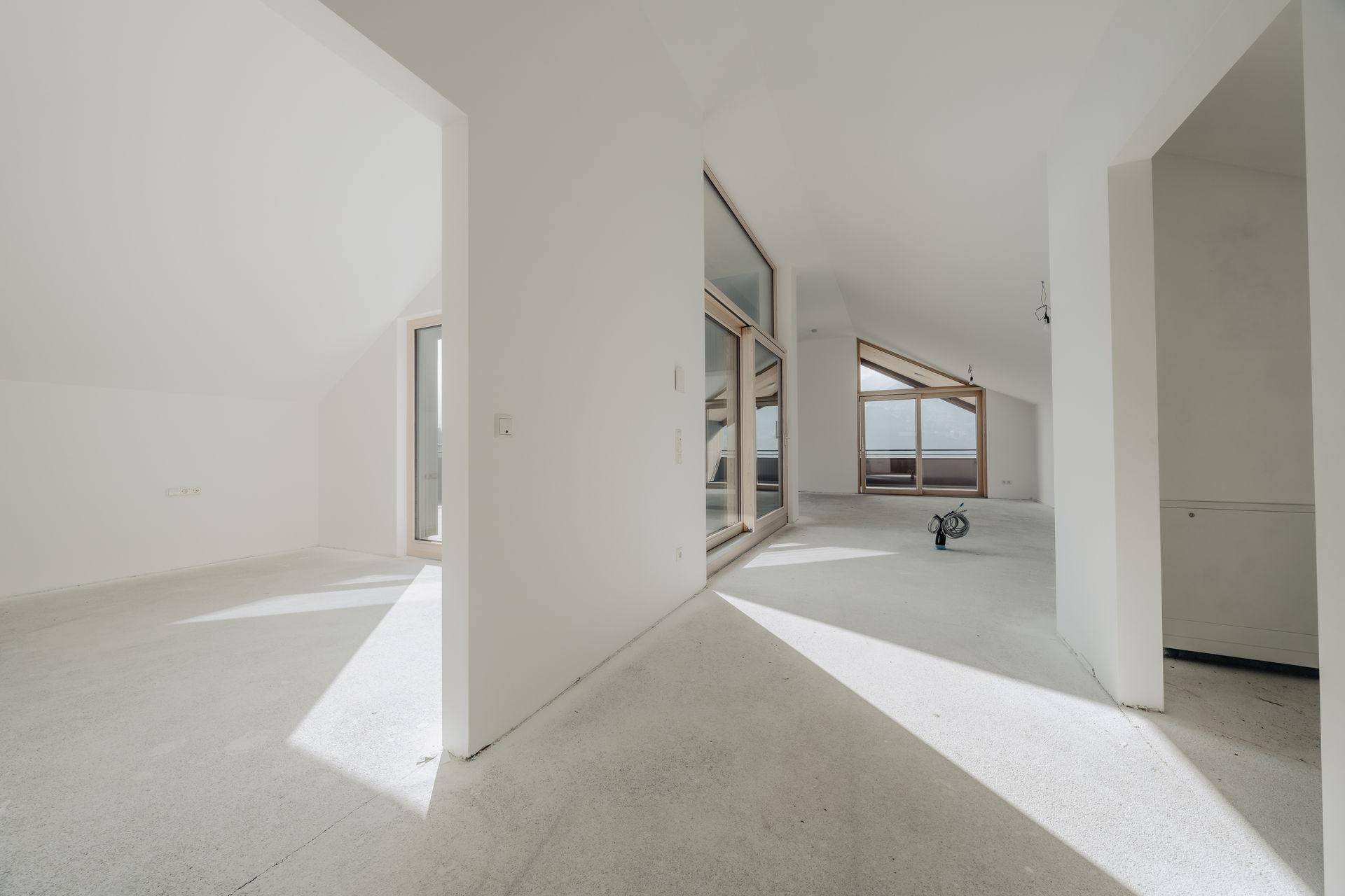 Heller, unfertiger Innenraum mit schrägen Decken und großen Fensterfronten im Neubau.