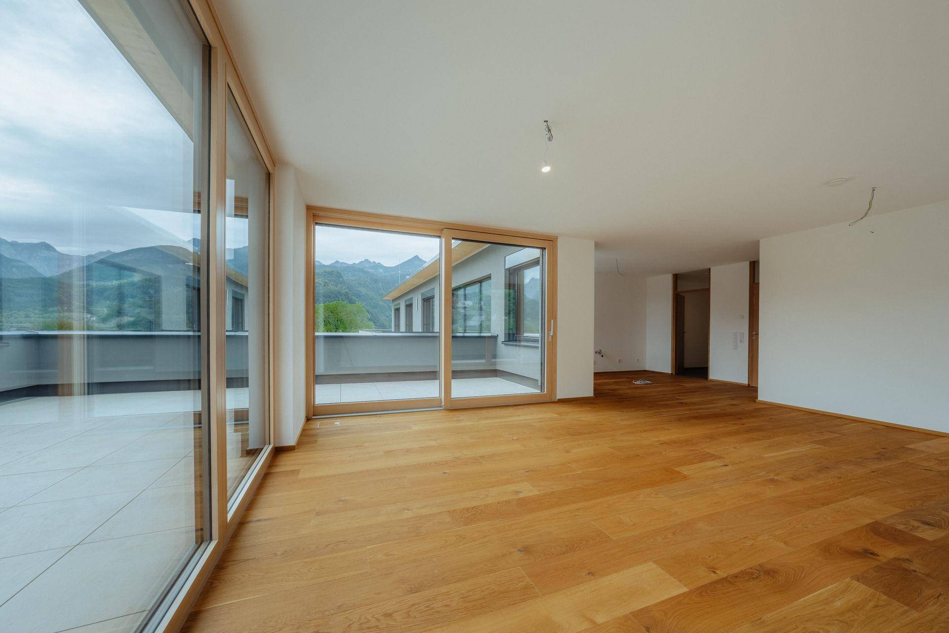 Heller Wohnraum mit Eichenparkett und großen Fenstern, die Zugang zu einer Terrasse mit Bergblick bieten.