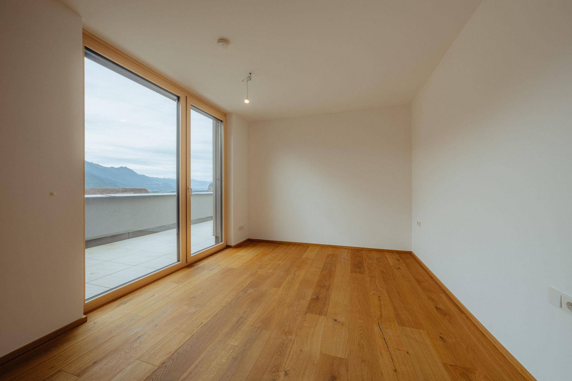 Geräumiges Schlafzimmer mit Holzboden und großen Fenstern, die Zugang zu einem Balkon mit Bergblick bieten.